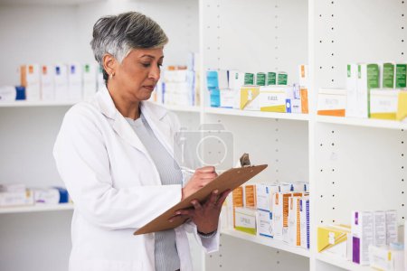Foto de Farmacéutica, medicina y una mujer escribiendo en un portapapeles en una farmacia para inventario o lista de verificación. Empleada madura comprueba estante para la gestión en la industria de la salud, farmacéutica y médica. - Imagen libre de derechos