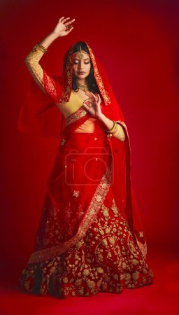 Photo for Fashion, dance and Indian woman in a traditional dress, jewellery and celebration on a red studio background. Female person, girl and model with a cultural outfit, dancing and routine with confidence. - Royalty Free Image