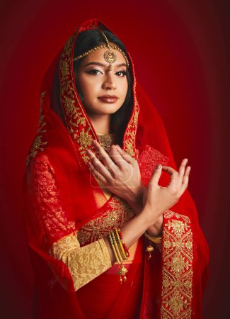 Téléchargez les photos : Mode, signe à la main et portrait de femme indienne avec voile dans les vêtements traditionnels, bijoux et sari. Religion culture, beauté et femme sur fond rouge avec accessoires, cosmétiques et maquillage. - en image libre de droit