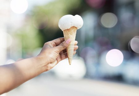 Photo for Hands, person and ice cream cone in city for dessert, cool snack and sweet food to enjoy outdoor. Closeup, scoop and frozen vanilla gelato in summer, travel and sunshine of urban town, street or trip. - Royalty Free Image