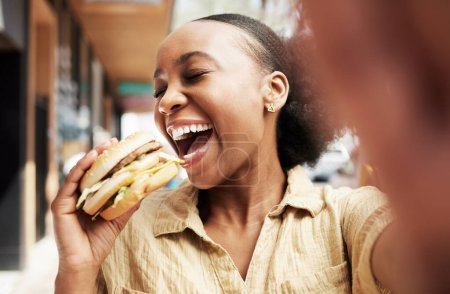 Photo for Burger, eating and woman in selfie, city and restaurant outdoor promotion, social media and live streaming review. Fast food, hungry and african person, customer or influencer with lunch photography. - Royalty Free Image