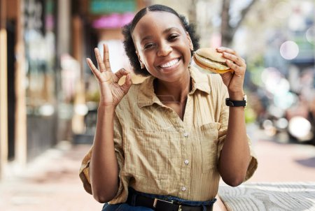 Photo for Burger, okay sign and portrait of woman in city, outdoor restaurant and happy customer experience or services. Fast food, like and excited african person with lunch review, excellence and yes emoji. - Royalty Free Image