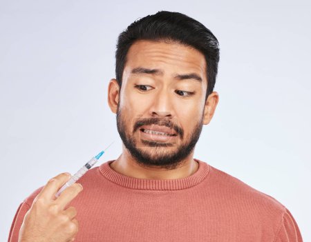 Photo for Fear, vaccine and face of asian man in studio with needle, phobia or covid scare on grey background. Corona, compliance and male person afraid of vaccination, medicine or prescription diabetic shot. - Royalty Free Image