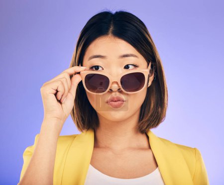 Photo for Fashion, sunglasses and a model asian woman on a purple background in studio for trendy style. Face, shades and attitude with a confident young female person looking over a stylish eyewear frame. - Royalty Free Image