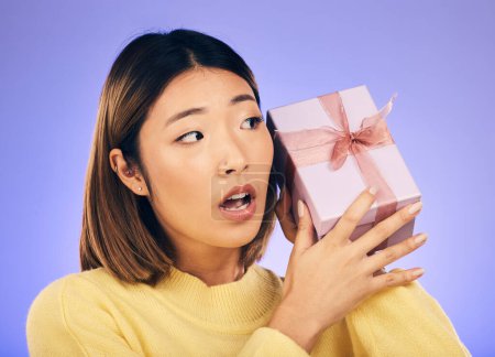 Photo for Thinking, gift and box with face of asian woman in studio for birthday, celebration and curious. Surprise, wow and party with female person and present on purple background for giveaway and package. - Royalty Free Image