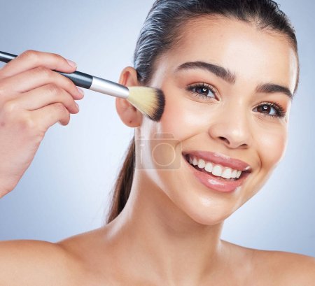 Beauty, cosmetic and portrait of woman with a makeup brush in studio for glamour facial routine. Self care, happy and young female model from Brazil with cosmetology face isolated by gray background