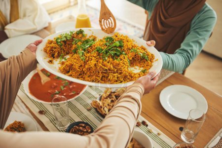 Foto de Cultura, Eid Mubarak y comida para la familia en la mesa para la celebración islámica, el festival y el almuerzo juntos. Ramadán, religión y por encima de las manos con comida, plato y cocina para ayunar, vacaciones y banquetes. - Imagen libre de derechos