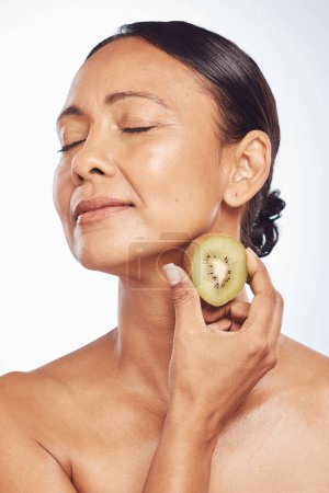 Photo for Relax, beauty or mature woman with kiwi for healthy detox, skincare or facial treatment routine in studio. Spa, face or senior model with wellness, self love or fruit isolated on white background. - Royalty Free Image
