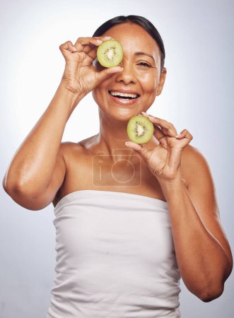 Photo for Skincare, portrait and senior woman with kiwi in studio isolated on a white background. Food, natural fruit and face of happy model with nutrition for wellness, healthy diet and anti aging for beauty. - Royalty Free Image