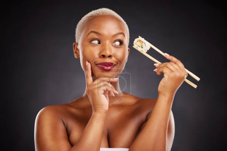 Photo for Sushi, thinking and face of a woman with chopsticks in studio for healthy eating, beauty or food. Black female model with makeup on dark background for wellness glow, diet or seafood advertising idea. - Royalty Free Image