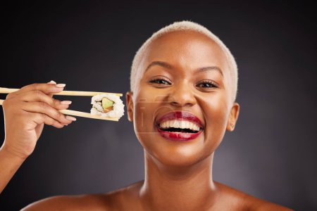 Photo for Face, woman and sushi with chopsticks in studio for healthy eating, beauty and food. Portrait of a happy black female model with makeup on a dark background for healthy eating, diet or seafood. - Royalty Free Image