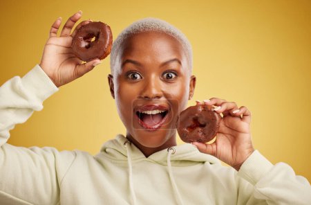 Téléchargez les photos : Portrait, chocolat et beignet avec une femme noire en studio sur fond d'or pour des bonbons ou une alimentation malsaine. Sourire, nourriture et cuisson avec une jeune femme heureuse tenant une pâtisserie sucrée pour le dessert. - en image libre de droit