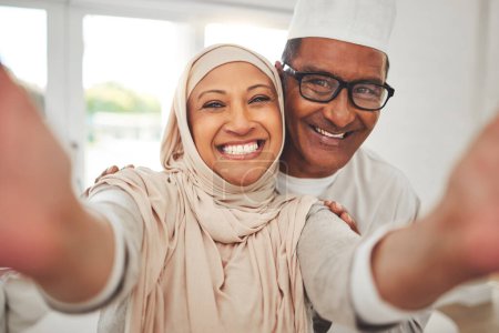 Téléchargez les photos : Selfie, Islam et vieux couple dans la maison avec le sourire, la culture heureuse et l'amour dans le salon en Indonésie. Mariage, homme et femme âgés dans le hijab sur le canapé dans le respect, la religion et le visage pour les médias sociaux - en image libre de droit