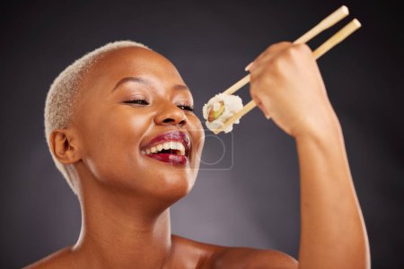 Photo for Face, eating and woman with sushi and chopsticks in studio for healthy food or beauty. Black female model with makeup on a dark background for wellness glow, fish diet or seafood with nutrition. - Royalty Free Image