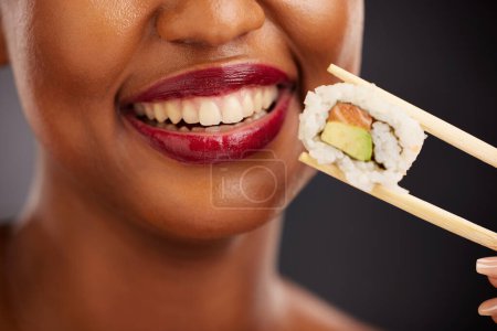 Photo for Mouth, eating and woman with sushi and chopsticks in studio for healthy food or teeth. Black female model with makeup on dark background for wellness glow, diet and seafood or salmon closeup. - Royalty Free Image