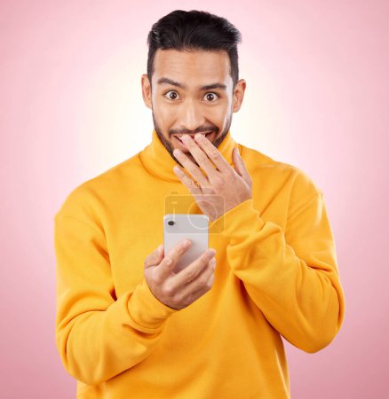 Photo for Phone, shock and portrait of a man in studio with a secret, gossip or fake news on social media. Male asian model with hand on mouth and smartphone for wow, surprise or chat on a pink background. - Royalty Free Image