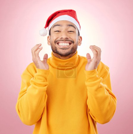 Téléchargez les photos : Portrait, homme excité et heureux avec chapeau de Noël, amusant et festif pour les vacances sur fond rose. Bonheur, célébration et modèle avec sourire, casquette de Père Noël et maillot de vacances d'hiver en studio. - en image libre de droit