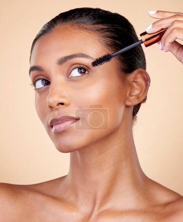 Photo for Face, mascara brush and woman, beauty and makeup with cosmetics tools isolated on studio background. Indian female model, cosmetology and skin glow, shine and eyelash extension with wellness. - Royalty Free Image