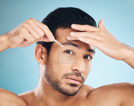 Photo for Man, face and eyebrow tweezers, beauty and skin, hair removal and cosmetics on blue background. Grooming, hygiene and male model, portrait and wellness with treatment, tools and self care in studio. - Royalty Free Image