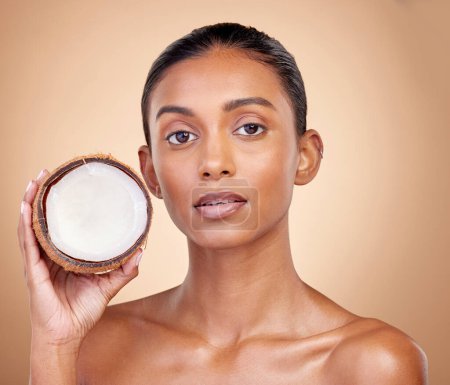 Photo for Woman face, coconut fruit and beauty, healthy skincare or vegan cream on brown studio background. Portrait of Indian person in natural product for dermatology, eco friendly cosmetics and oil benefits. - Royalty Free Image