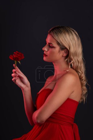 Téléchargez les photos : Beauté, mode et femme avec une rose sur fond noir foncé dans un studio pensant à l'amour, à la romance ou à l'esthétique rouge. Fille avec une fleur, robe et style formel dans la fantaisie, conte de fées ou d'art. - en image libre de droit