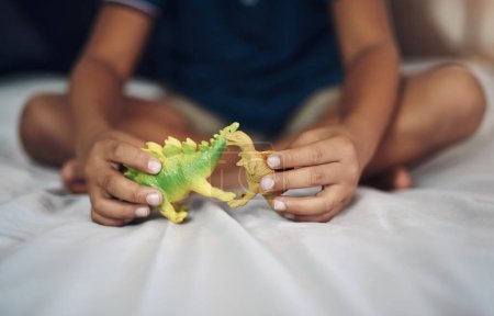 Foto de Ojalá aún existieran los dinosaurios. Recortado disparo de un niño irreconocible jugando con dinosaurios mientras está sentado en su cama - Imagen libre de derechos