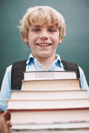Photo for I cant wait to read them all. A cute young boy carrying a large stack of books and smiling at you - Royalty Free Image