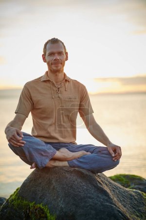 Foto de La felicidad está aquí, ahora mismo. Tiro de un hombre sentado en la posición de loto durante su rutina de yoga en la playa - Imagen libre de derechos