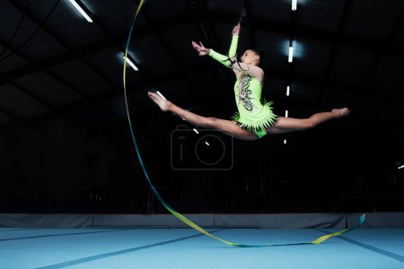 Photo for Jump, rhythmic gymnastics and woman in gym with ribbon, creative sport or action, performance or fitness. Competition, athlete and female gymnast, dance and art with body, routine and energy at arena. - Royalty Free Image