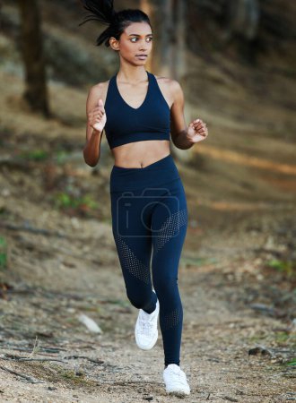 Photo for Woman is running in forest, fitness and cardio in nature with exercise and healthy, active lifestyle. Female runner outdoor, training for marathon with speed, energy and workout for health and sport. - Royalty Free Image