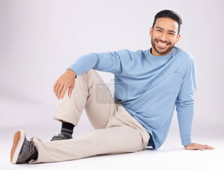 Photo for Portrait, fashion and happy man on the floor in studio isolated on a white background. Style, smile and Asian person from Cambodia in casual clothes, trendy aesthetic or confidence to relax on ground. - Royalty Free Image
