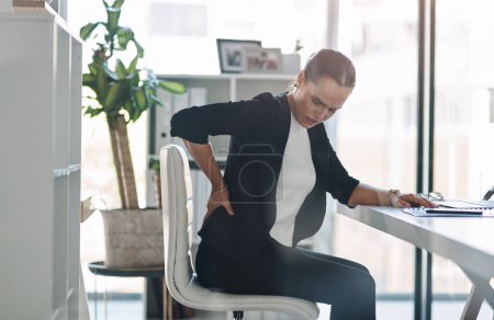 Photo for These long hours are starting to negatively affect her health. Cropped shot of an attractive young businesswoman suffering from back pain while working inside her office - Royalty Free Image