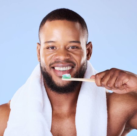 Photo for Portrait, black man and brushing teeth in studio for dental, bamboo toothbrush and blue background. Face of male model cleaning mouth with eco friendly wooden product for fresh breath or oral hygiene. - Royalty Free Image