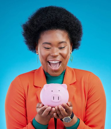 Photo for Woman, piggy bank and wow for savings, financial investment and profit, increase or budget success. Excited african person with banking goals, finance safe and container on a blue, studio background. - Royalty Free Image