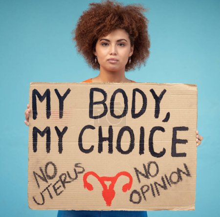 Black woman, portrait and poster to protest abortion, body choice and freedom of human rights in studio. Feminist, rally and sign for safe decision, equality and support of justice on blue background.