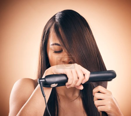 Young woman, hair care and flat iron in studio to straightener for healthy shine and growth. Young female aesthetic model on a brown background with hot tools for hairstyle, cosmetics and beauty.