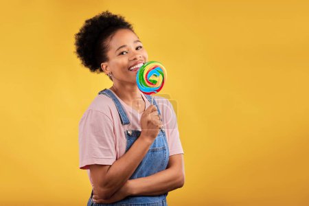 Téléchargez les photos : Joyeux, bonbons et portrait d'une femme noire avec une sucette sur un fond de studio pour la nourriture. Sourire, maquette et une fille africaine ou un modèle avec des bonbons pour le dessert isolé sur un fond d'espace. - en image libre de droit