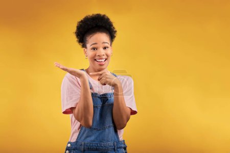 Photo for Portrait, marketing and a black woman pointing to her palm for the promotion of a product on a yellow background in studio. Smile, advertising or space with a happy young female brand ambassador. - Royalty Free Image