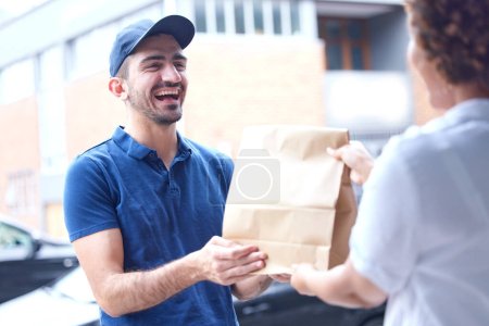 Photo for Happy man, delivery and paper bag in the city for courier service, fast food or online shopping at the door. Male person giving customer parcel, package or order for transport, logistics or ecommerce. - Royalty Free Image