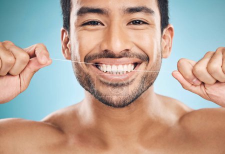 Photo for Wellness, teeth and flossing of a man portrait with cleaning and dental health in a studio. Face, blue background and healthy male person with dental floss for mouth hygiene and healthcare with smile. - Royalty Free Image