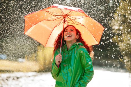 Téléchargez les photos : Drôle, nature ou femme heureuse avec un parapluie sous la pluie pour l'assurance ou la couverture en ville à l'extérieur. Sourire, bonheur ou fille humide riant avec des outils pour la couverture hivernale, la protection et la marche dans un parc. - en image libre de droit
