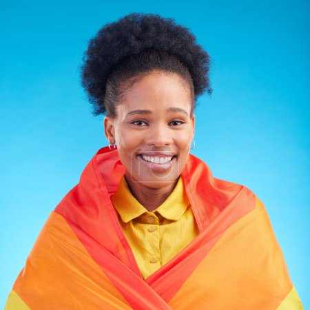 Téléchargez les photos : Fierté, drapeau et portrait de femme noire en studio pour gay, droits et style de vie lgbtq sur fond bleu. Arc-en-ciel, liberté et visage de lesbiennes africaines heureuses, souriantes et confiantes avec sexualité. - en image libre de droit
