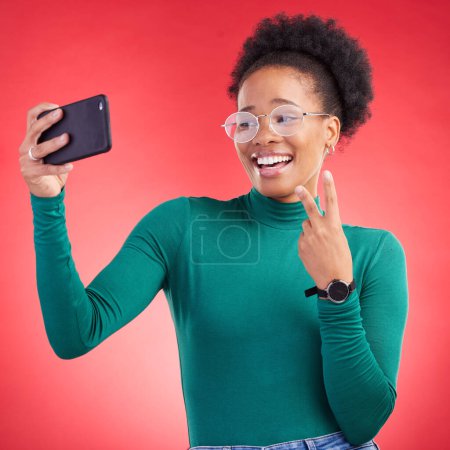 Photo for Happy black woman, peace sign and selfie for photography against a red studio background. African female person or model smile for photograph, memory or social media and online post in happiness. - Royalty Free Image