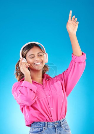 Photo for Happy woman, headphones and listening to music, audio streaming service and techno or student podcast in studio. Young person dance to radio for wellness and electronics on a blue gradient background. - Royalty Free Image