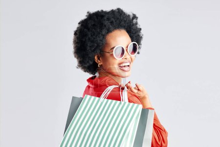 Foto de Mujer negra feliz, afro y bolsas de compras para descuento, venta o acuerdo de moda en un fondo de estudio blanco. Retrato de una mujer africana, cliente o comprador sonrisa para la compra en la felicidad. - Imagen libre de derechos