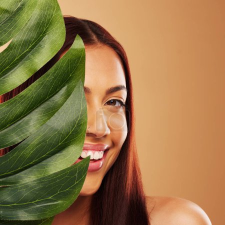 Photo for Leaf, beauty and portrait of a happy woman in studio for natural dermatology, cosmetics or wellness. Skin care, nature and monstera plant for eco friendly facial of model person on brown background. - Royalty Free Image
