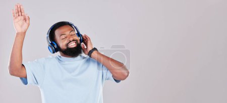 Photo for Headphones, happy and young man in a studio listening to music, playlist or album while dancing. Happiness, smile and African male model streaming song or radio by gray background with mock up space - Royalty Free Image
