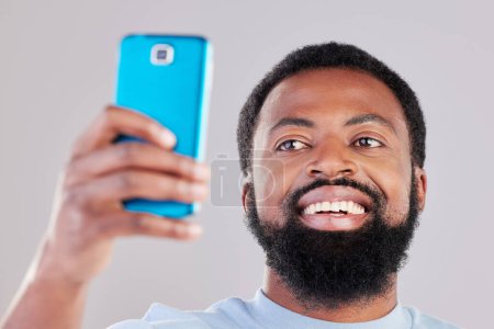 Téléchargez les photos : Heureux homme noir, visage et selfie en photographie pour les médias sociaux, vlog ou réseautage sur fond de studio gris. Homme africain sourire pour photo, mémoire ou communication en ligne et image. - en image libre de droit