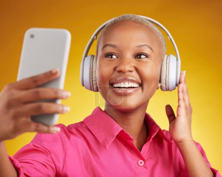 Téléchargez les photos : Selfie, sourire et femme noire avec écouteurs de musique en studio, streaming ou abonnement sur fond jaune. Podcast, photo de profil et influenceur de médias sociaux dame en ligne pour la radio ou un billet de blog. - en image libre de droit