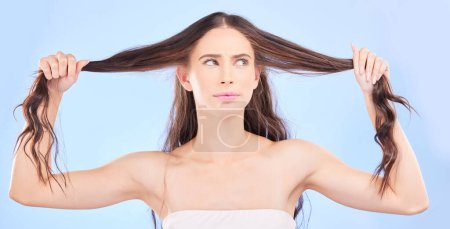 Photo for Thinking, woman and damaged hair in studio with cosmetics, haircare or confused face for beauty, problem or split ends. Frustrated, girl and ideas for hairstyle in salon or growth on blue background. - Royalty Free Image
